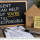 Property management graphic showing a chalkboard message that an agent can help but the investor is still responsible, alongside a wooden house model, buy-to-let keys and a property management checklist on a desk
